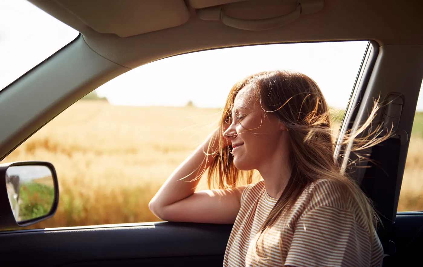 Mujer sonriendo con el viento en el cabello desde la ventana de su carro
