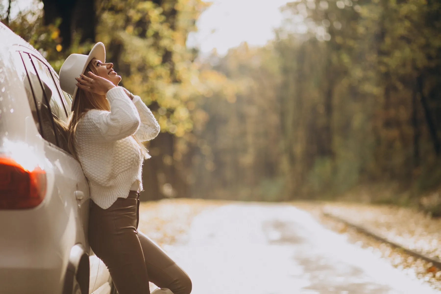 Mujer sonriendo recostada en su carro en un camino rodeado de árboles