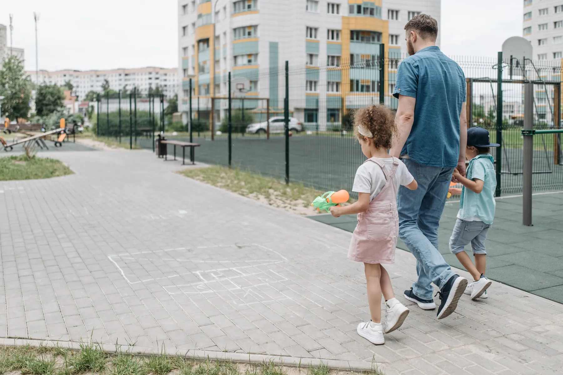 Un papá camina de la mano con sus dos hijos por un parque
